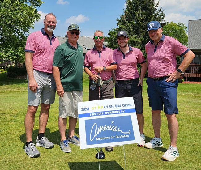 Golfers posing by a sponsored hole sign at the 2024 Starfysh Golf Classic.